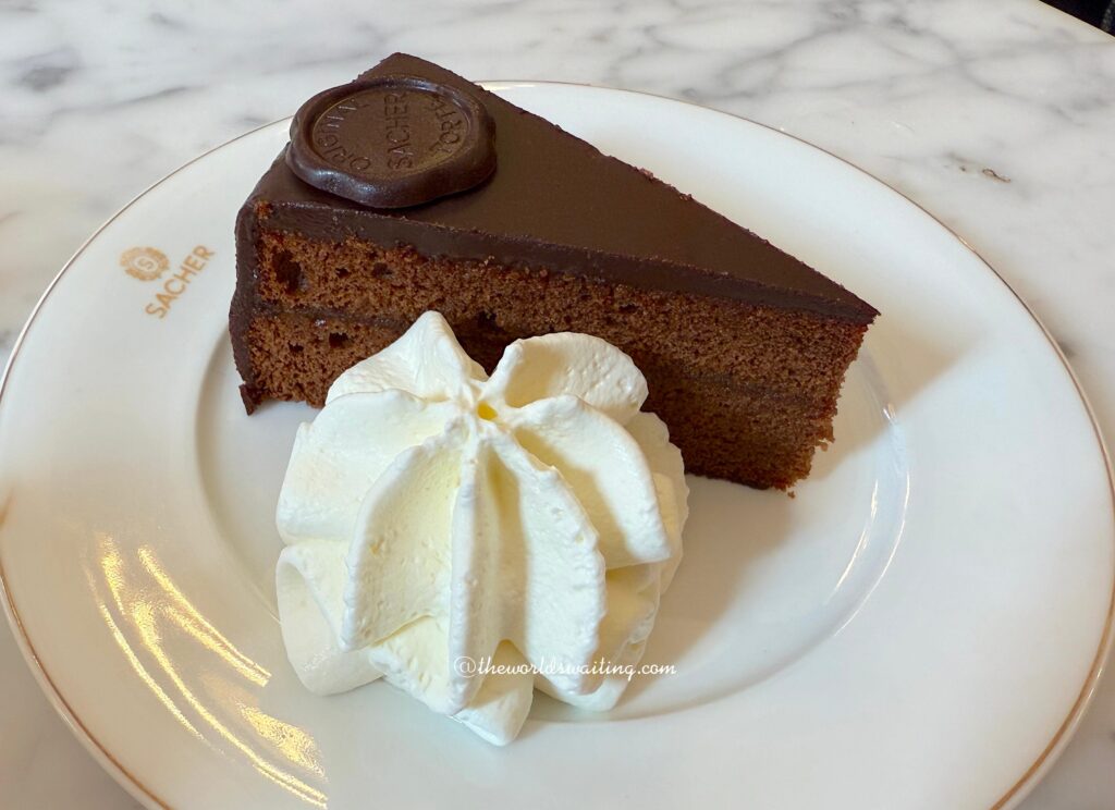 Traditional Sachertorte is an Austrian chocolate cake featuring apricot jam and chocolate glaze, served here with whipped cream